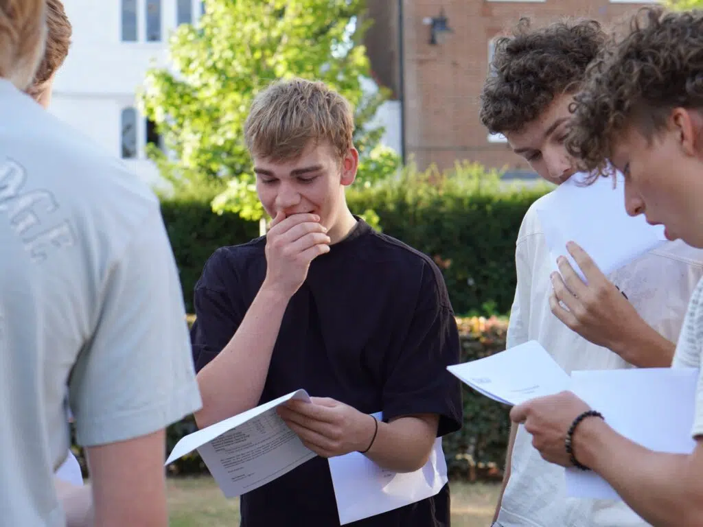 Group of teens outside, reading papers and discussing together while standing in a garden area.
